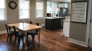 A modern kitchen with a central island, black cabinets, and a dining area with a wooden table and chairs. - 1.3 Mile Walk to the Augusta National Clubhouse!<br>Lovely Cottage with Space! (Augusta)