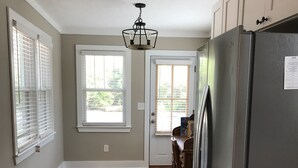 A kitchen with wooden flooring, white cabinets, a refrigerator, and a window with blinds. - 1.3 Mile Walk to the Augusta National Clubhouse!<br>Lovely Cottage with Space! (Augusta)