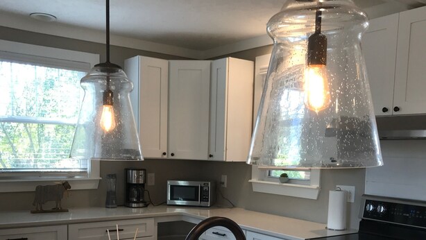 A modern kitchen with white cabinets, a black faucet, and a marble countertop. There are two pendant lights with exposed bulbs, a stainless steel microwave, and a black stove. - 1.3 Mile Walk to the Augusta National Clubhouse!<br>Lovely Cottage with Space! (Augusta)