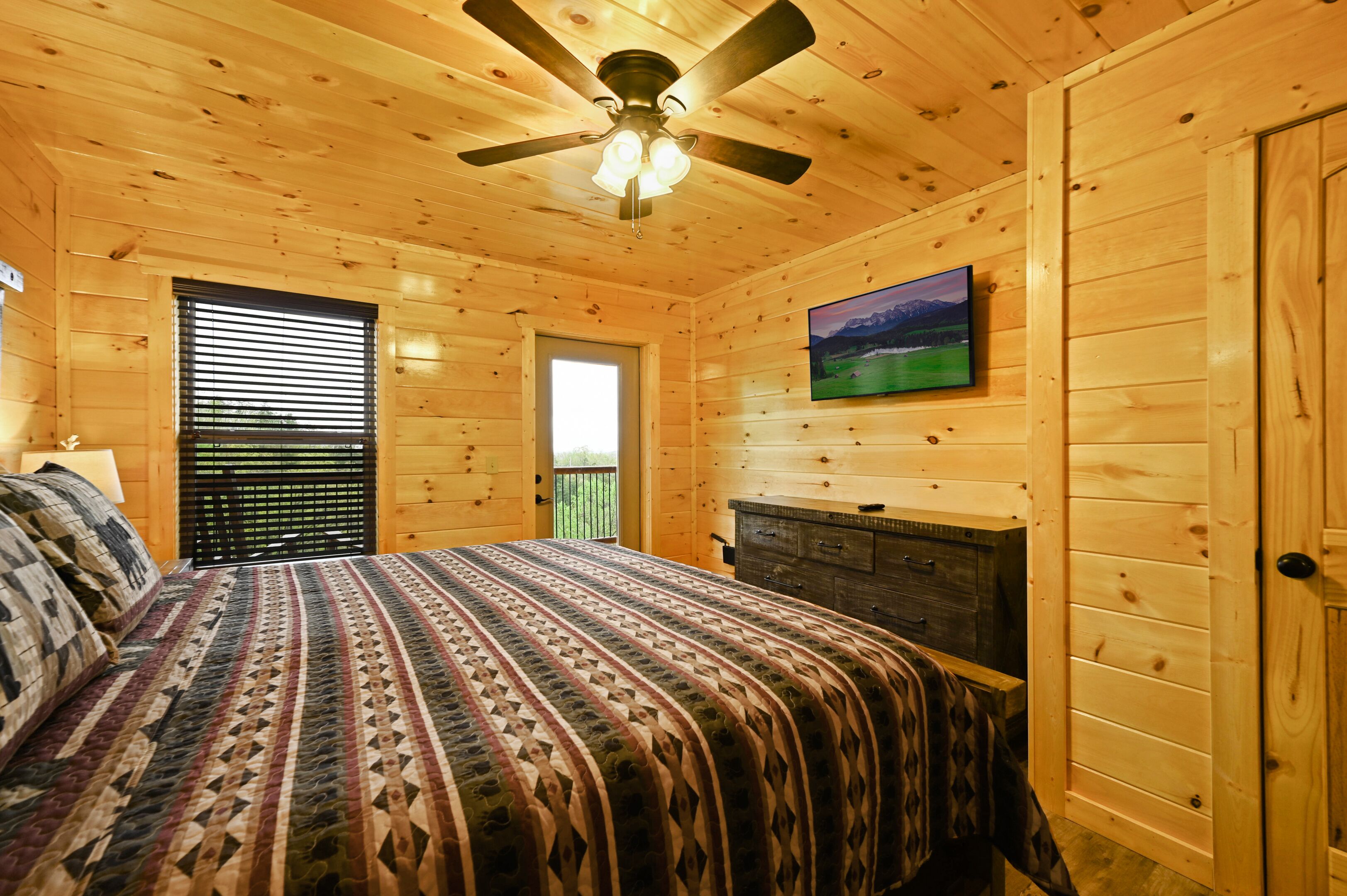 A wooden cabin bedroom with a bed, a ceiling fan, a fireplace, and a window with blinds.