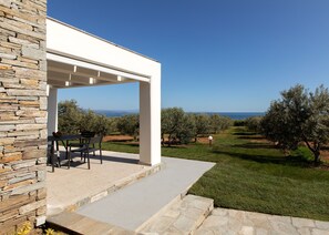 A covered outdoor seating area with a stone wall, a table, and chairs. - Casa Del Olivar (Aristotelis)