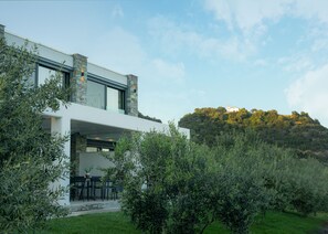 A modern house with a stone facade, a patio with outdoor furniture, and a view of a hill with a building on top.