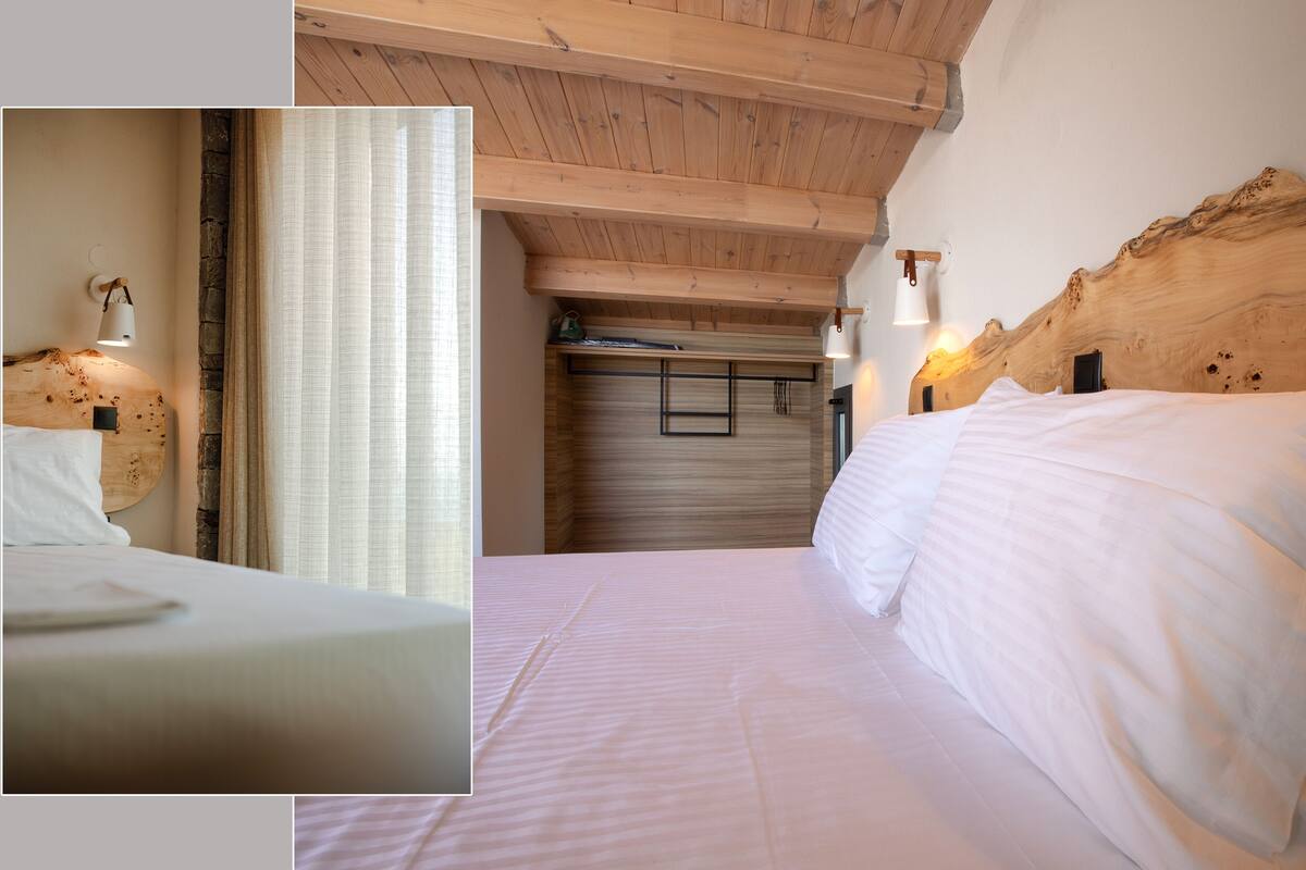 Habitación de hotel con techo de madera, cama con ropa blanca, cabecero de madera e iluminación empotrada en la pared.