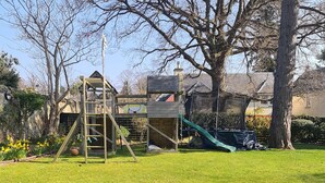 A wooden play structure with a slide and a climbing ladder in a backyard.