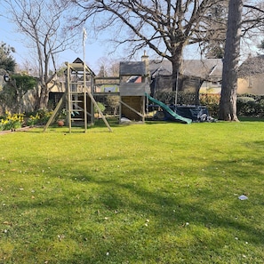 Explore a backyard with a play structure featuring a slide and climbing ladder, surrounded by a lush lawn and trees.