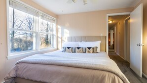 Un dormitorio con una cama grande, una ventana con persianas y una puerta que da a otra habitación.