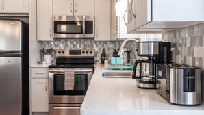 Una cocina moderna con electrodomésticos de acero inoxidable, armarios blancos y salpicadero de azulejos.