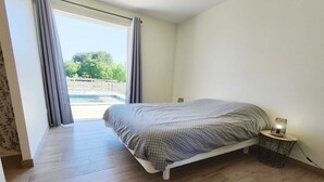 Un dormitorio con cama, lámpara de noche y vista a una piscina a través de un ventanal.