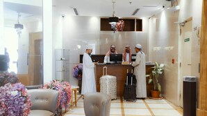 Een hotel receptie met een receptiebalie, vier medewerkers, een computer en een potplant.