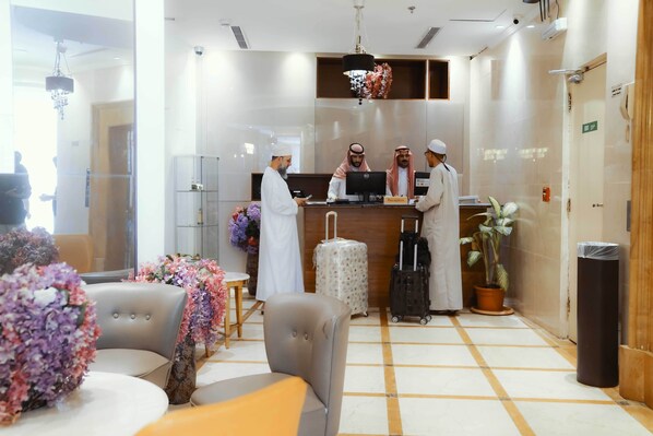 A hotel reception area with a reception desk, four staff members, a computer, and a potted plant. - Nour Al Thuria Hotel (Makkah)