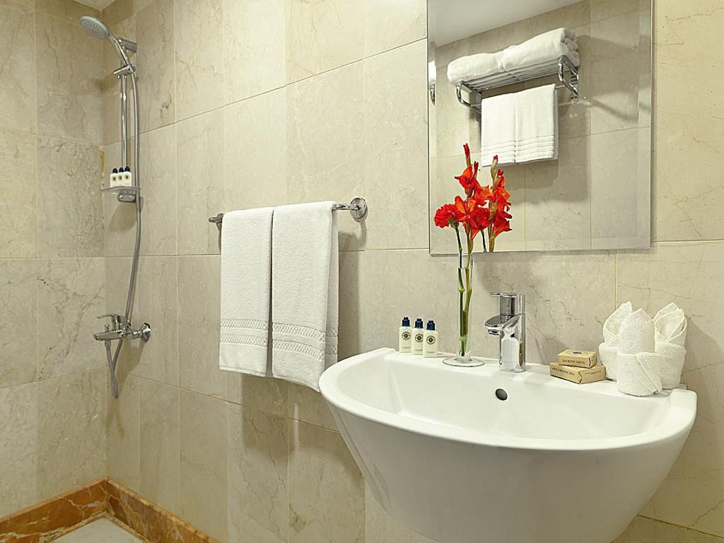 Une salle de bain avec un lavabo blanc, un miroir, un porte-serviettes et une douche.