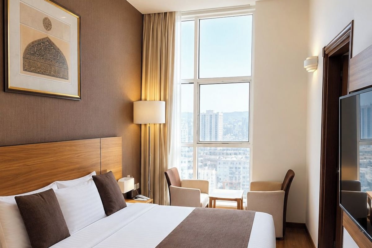A hotel room with a large bed, a TV, a desk, and a window with a city view.