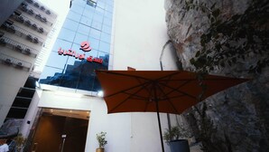 Een hotelgevel met modern glas, een grote parasol en potplanten.
