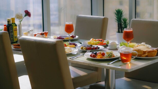 Een ontbijtsetting met een tafel gedekt voor twee personen, met schalen fruit, toast en drankjes.