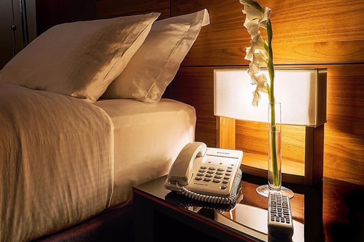 Een hotelkamer met een bed, een bedtafeltelefoon, een lamp en een vaas met bloemen.
