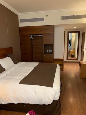 A hotel room with a large bed, wooden headboard, built-in wardrobe, and a small seating area with a table and chair. - Nour Al Thuria Hotel (Makkah)