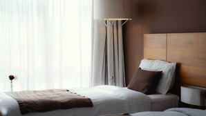 Een hotelkamer met twee bedden, een groot raam met dunne gordijnen, een bedlamp en een houten hoofdeinde.
