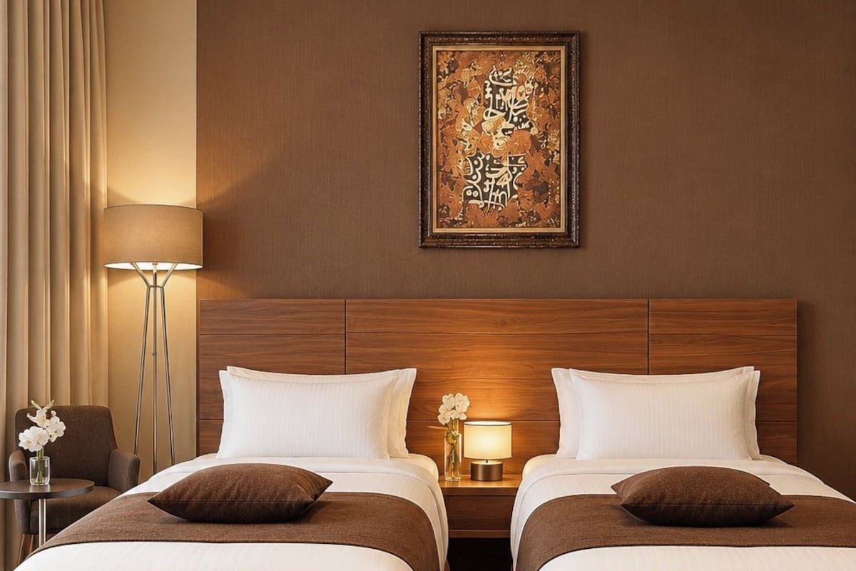 A hotel room with two beds, a nightstand with a lamp, a wall-mounted artwork, and a floor lamp.