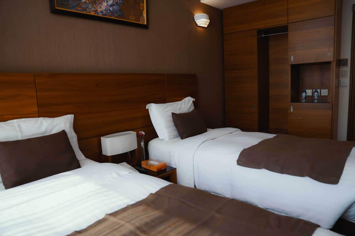 Een hotelkamer met twee bedden, houten hoofdeinden, een nachtkastje met een lamp en een schilderij aan de muur.
