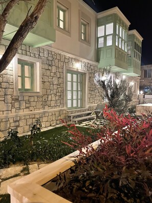 Un bâtiment en pierre doté de nombreuses fenêtres et d’un balcon, entouré d’un jardin bien entretenu où poussent différentes espèces de plantes.