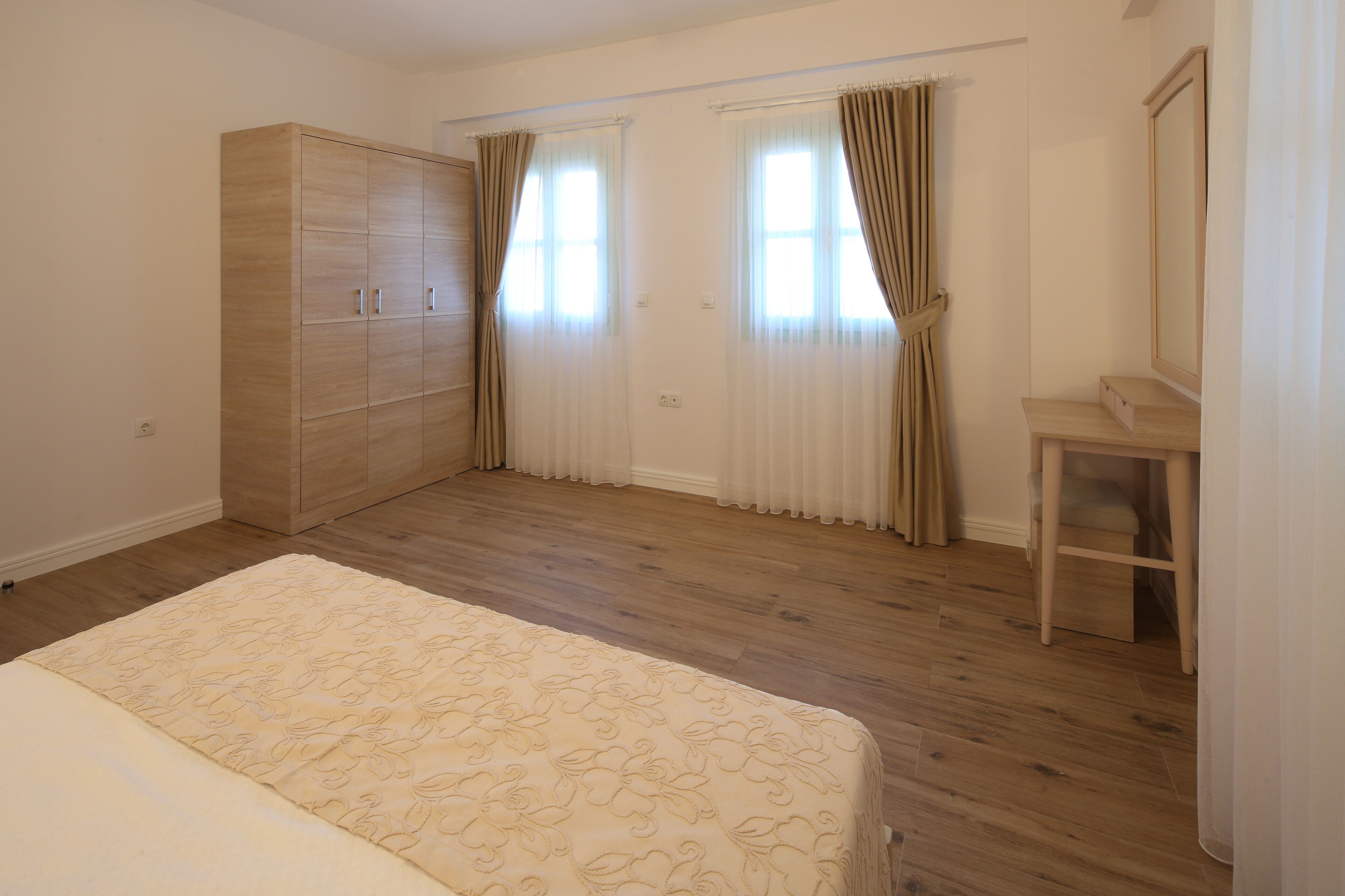 Un dormitorio con un armario de madera, una cama con colcha floral, una pequeña mesa de madera y un espejo.