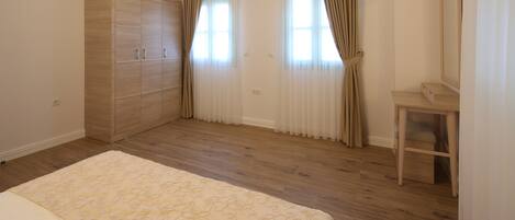 Un dormitorio con un armario de madera, una cama con colcha floral, una pequeña mesa de madera y un espejo.
