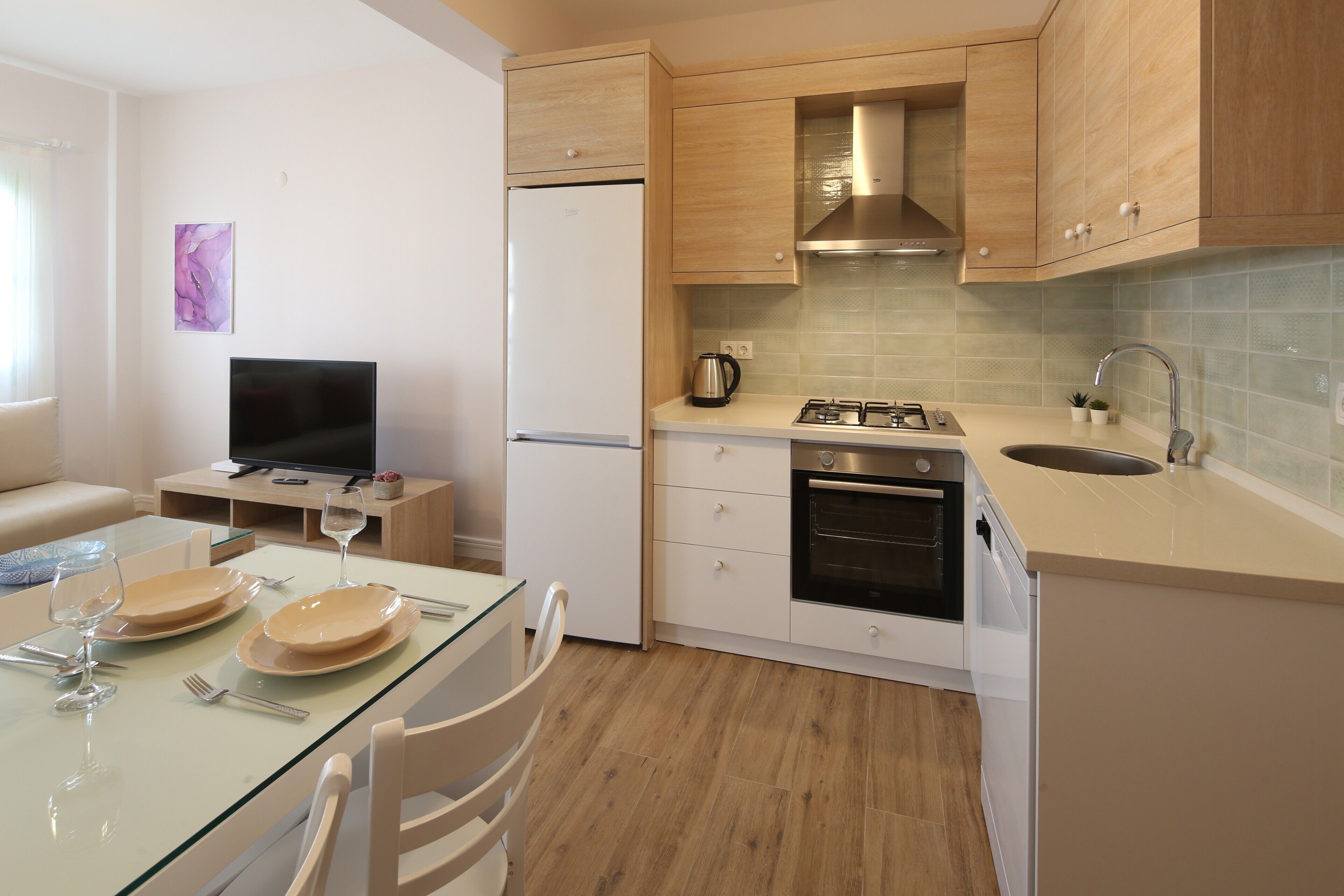 A compact kitchen with a refrigerator, stove, sink, and a dining area with a glass table and chairs.
