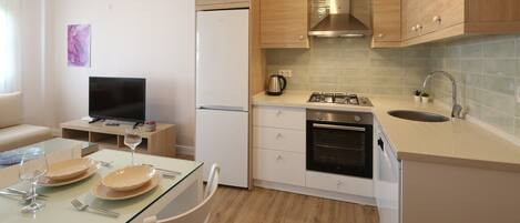 A compact kitchen with a refrigerator, stove, sink, and a dining area with a glass table and chairs.