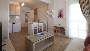 A modern kitchen with white cabinets, a dining area with a glass table, and a cozy living space with a sofa. - Cigdem'inn Sigacik (Seferihisar)