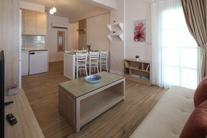 Uma cozinha moderna com armários brancos, uma área de jantar com mesa de vidro e uma sala de estar aconchegante com um sofá.