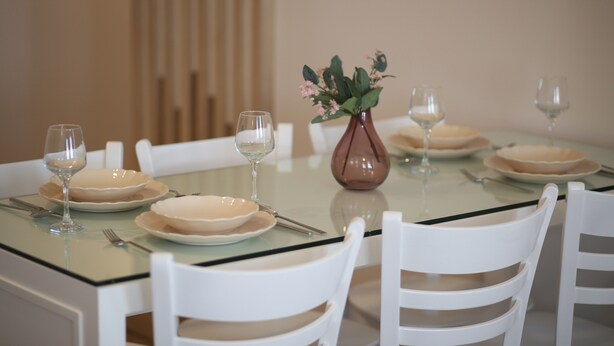 A dining table set with plates, glasses, and cutlery, surrounded by white chairs. - Cigdem'inn Sigacik (Seferihisar)