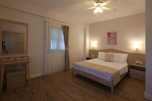 Une chambre d’hôtel équipée d’un lit, de tables de chevet, d’un bureau, d’un miroir et d’un ventilateur de plafond.
