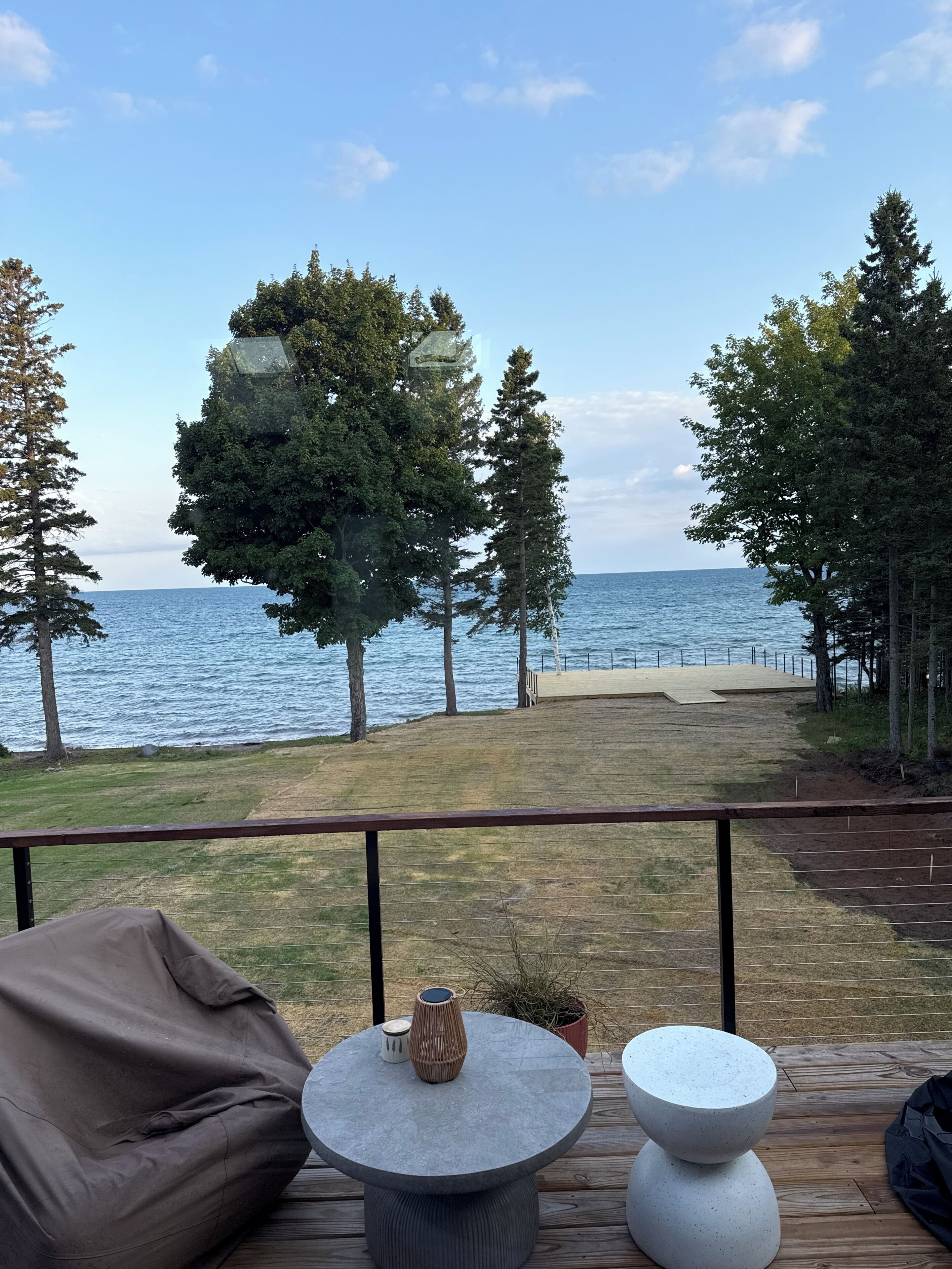 A deck with a view of the sea, a round table, a bean bag, and a potted plant.