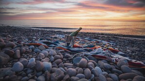 A beach scene with a blanket, a bottle, and a cooler on pebbles. - Lake Superior premium bespoke accommodations with ultimate view! (Calumet Township)