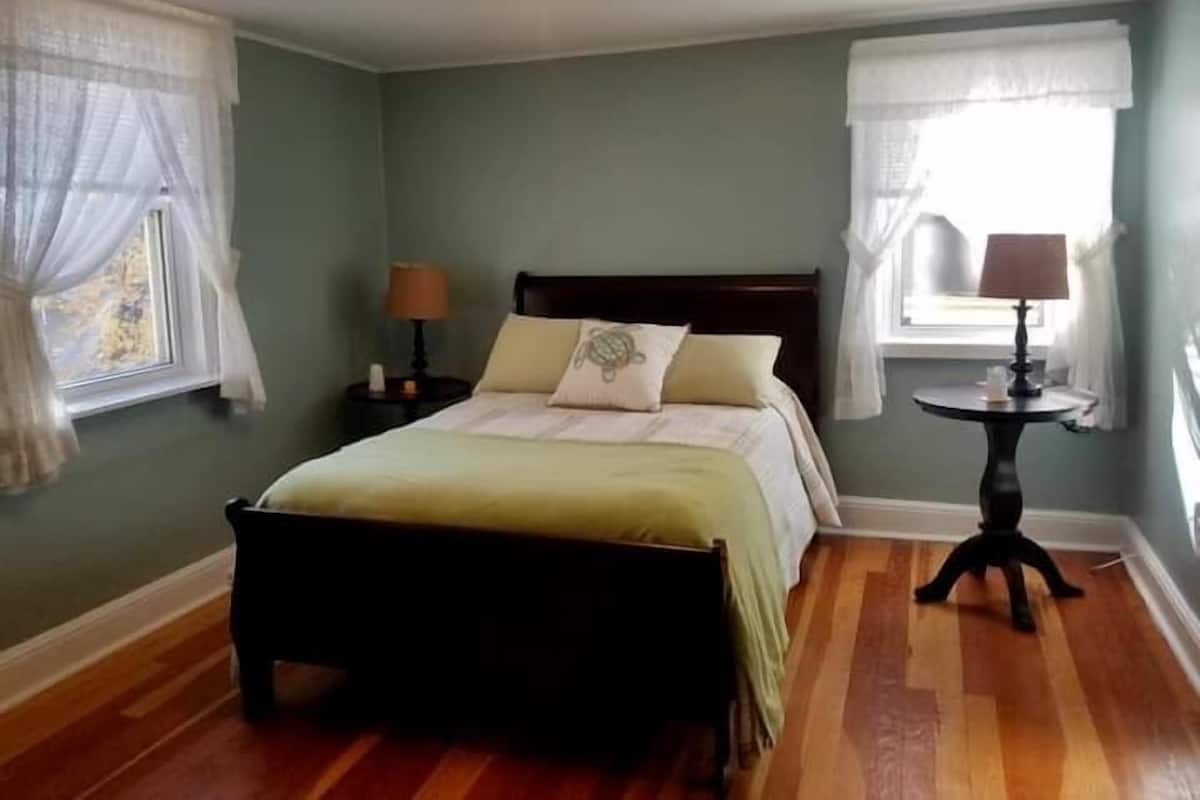 Een slaapkamer met een bed, een nachtkastje, een lamp en een raam met gordijnen.