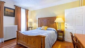 A bedroom with a wooden bed, two bedside tables with lamps, a radiator, and a door. - Sunny Home B&B (Charlottetown)