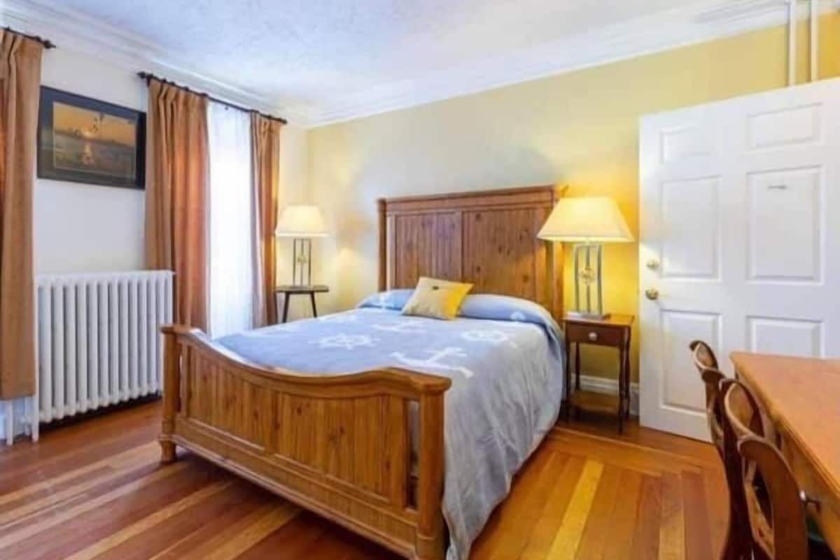 Een slaapkamer met een houten bed, twee nachtkastjes met lampen, een radiator en een deur.