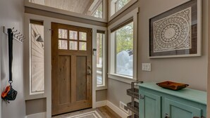 Un pasillo con una puerta de madera, un mueble de color verde agua, un adorno en la pared y una ventana con vistas a la nieve.