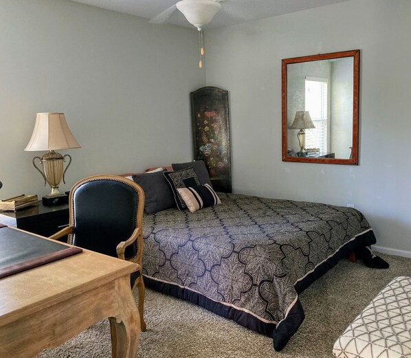Un dormitorio con cama, una silla, un escritorio, una lámpara y un espejo.