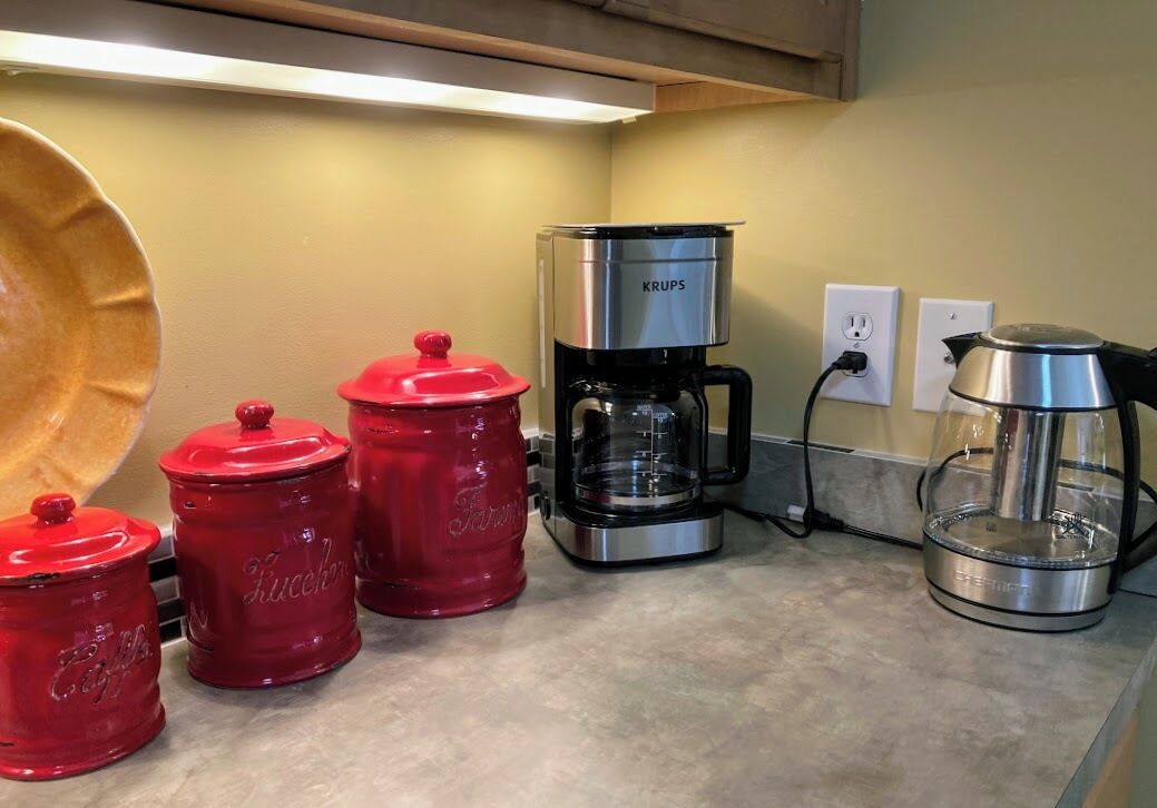A kitchen counter with a coffee maker, a kettle, and red containers.