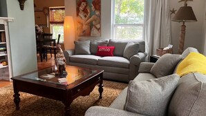Sala de estar con sofá, una mesa de centro y una lámpara. Hay una ventana con cortinas y un cuadro en la pared.