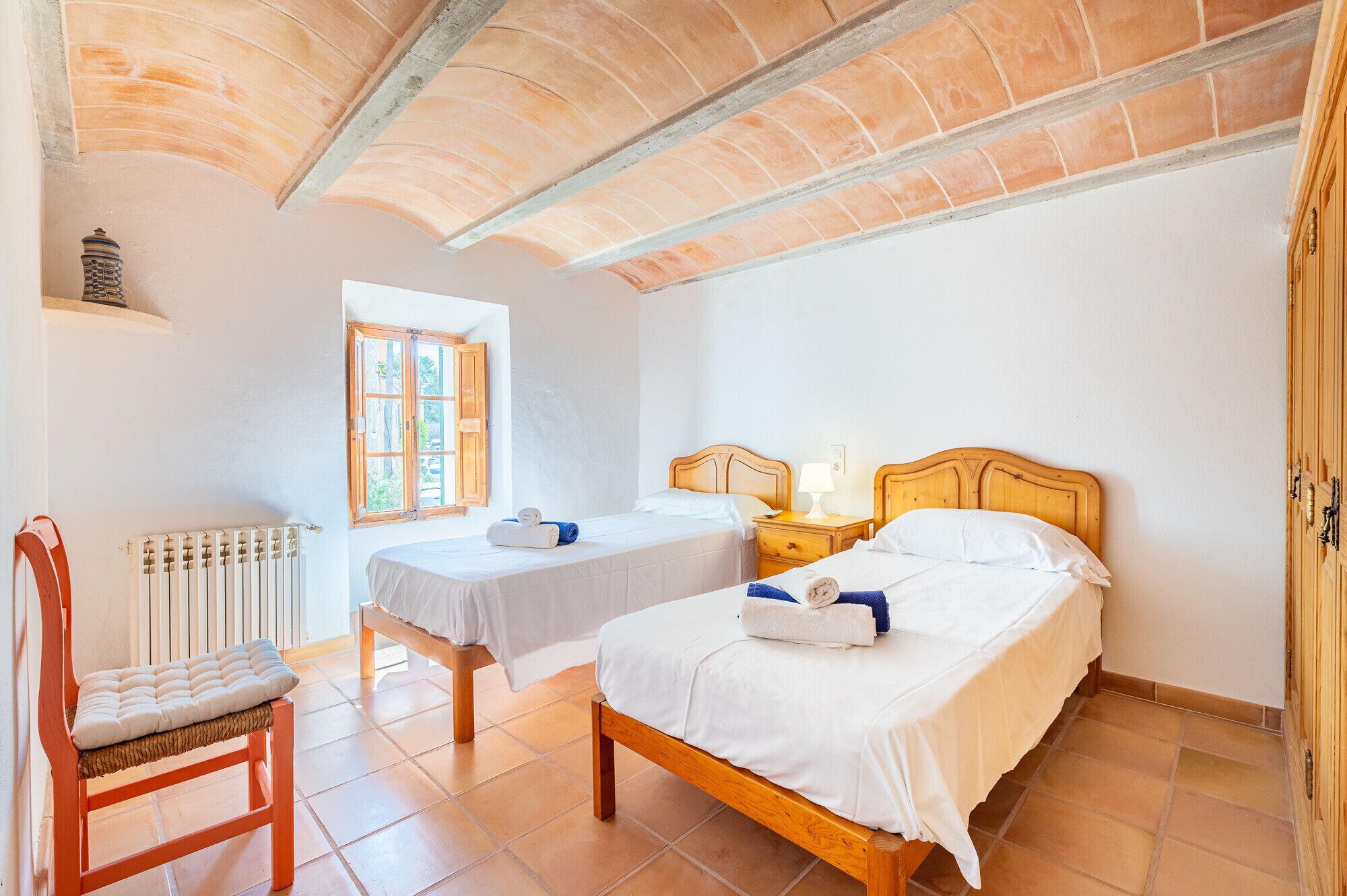 Camera da letto con due letti, una sedia di legno, una finestra, un termosifone e una lampada.