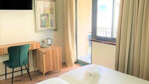 Habitación de hotel con dos camas, un escritorio, una silla, un televisor y una ventana con cortinas.