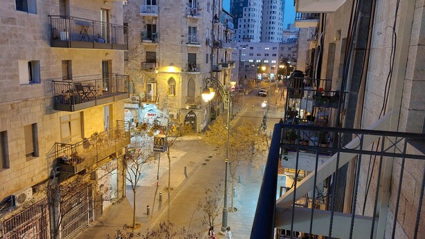 Un edificio de varios pisos con balcones, una calle arbolada y un letrero de McDonald's.