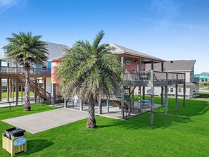 Une propriété située en bord de mer, dotée d’une terrasse en bois, de palmiers et offrant une vue sur un ciel dégagé.
