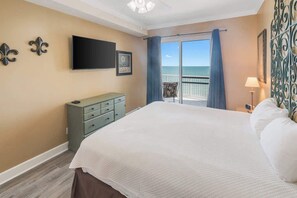 Une chambre dotée d’un grand lit, d’un téléviseur à écran plat, d’une commode et d’un balcon offrant une vue sur l’océan.