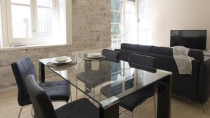 A modern living room with a glass dining table, black sofas, and a TV. - Bravissimo Cort Reial 2A, beautifully renovated (Girona)