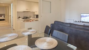 A modern living room with a glass dining table, a dark leather sofa, and a kitchen area in the background. - Bravissimo Cort Reial 2A, beautifully renovated (Girona)
