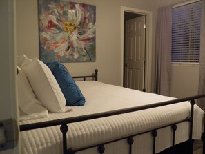 A bedroom with a bed, a painting on the wall, and a door leading to another room.