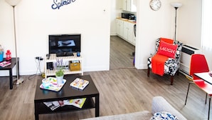 Un salon moderne avec un téléviseur, une table basse, un canapé et un fauteuil rouge agrémenté d’un coussin sur lequel est écrit le mot « RIRE ».